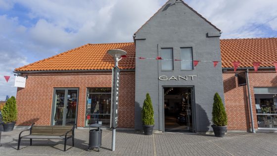 Mand og kvinde sidder på græsset, lænet op af en stenmur, iført Gant shorts, bukser og poloer. Inspirationsbillede til at købe Gant tøj i Ringsted Designer Outlet
